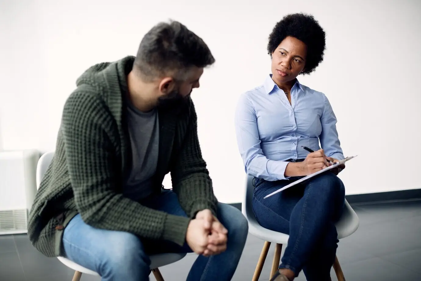 Zwarte vrouwelijke psychotherapeut maakt aantekeningen terwijl ze met een man praat tijdens een counselingsessie.